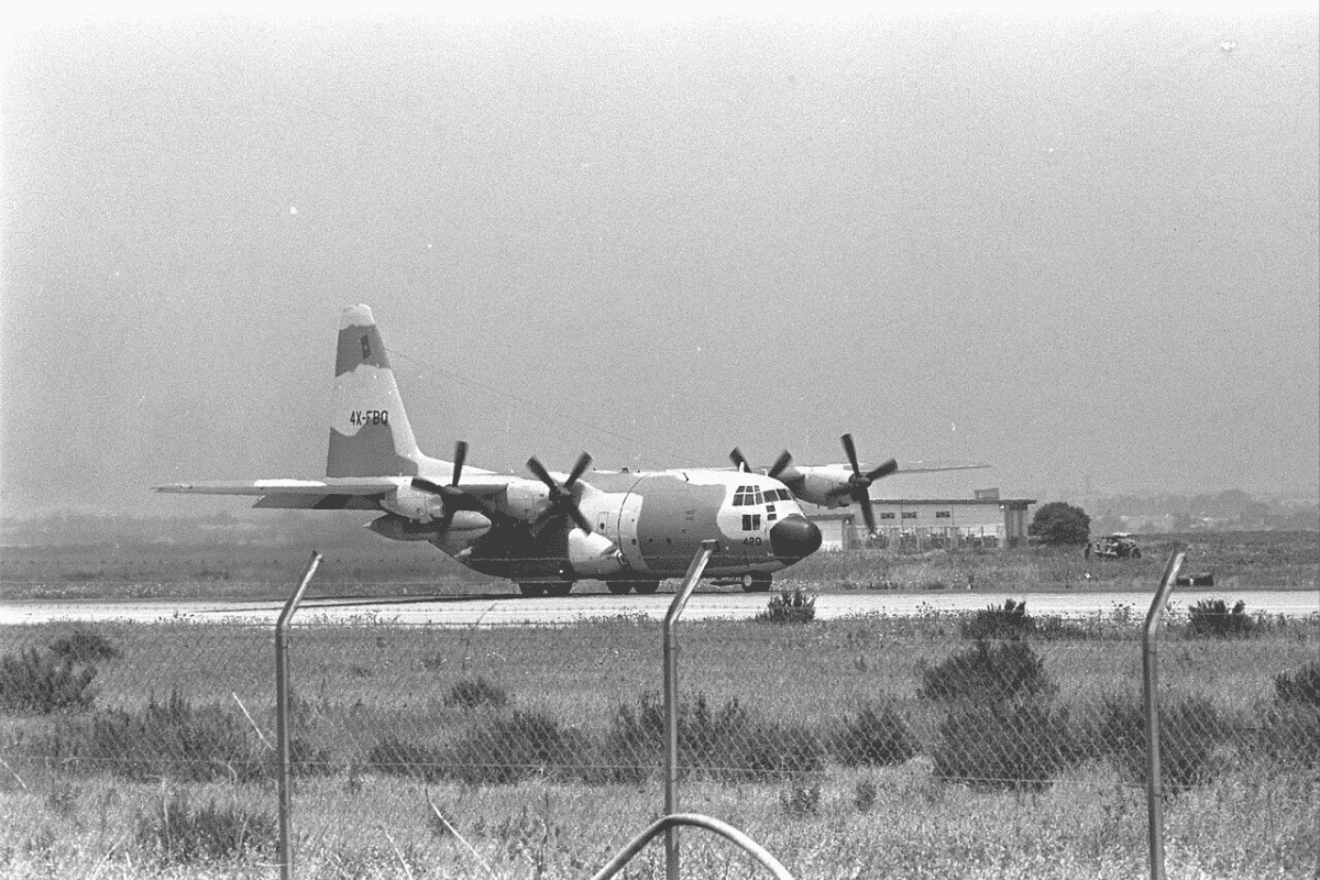 Историческое черно-белое фото транспортного самолета C-130 Hercules, стоящего на взлетно-посадочной полосе, вероятно, в Израиле.