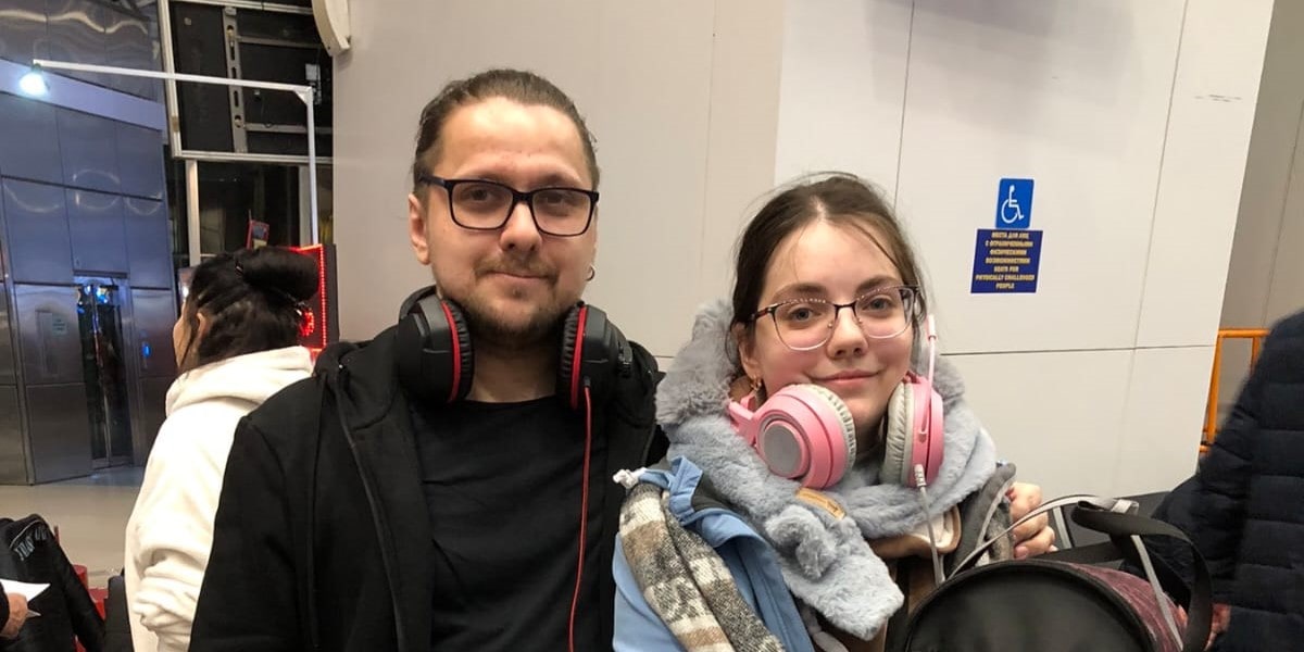 Мужчина и девушка с наушниками стоят вместе в помещении, улыбаясь в камеру.