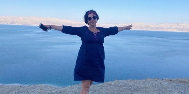 Женщина стоит на фоне моря с раскинутыми руками и улыбается.
